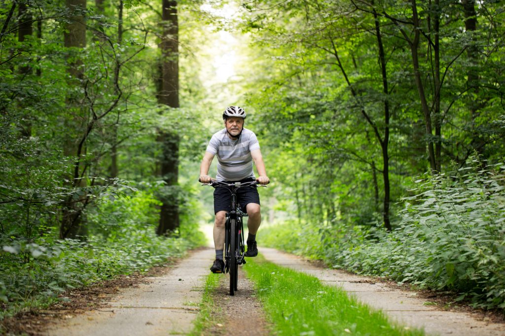 Senior man on a bike during lovely summer time in forest, smiling, enjoying trip