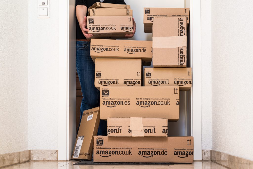 OSTFILDERN-SCHARNHAUSEN, GERMANY - MAY 18, 2014: A woman is picking up a large stack of parcels by Amazon.com in different sizes waiting in front of the entrance door to her flat on May, 18, 2014 in Ostfildern-Scharnhausen near Stuttgart, Germany. This conceptual photo can serve different purposes: It might demonstrate the domination of Amazon.com in the area of online shopping or the trend in general to shop online for all the different items you need in your personal life.