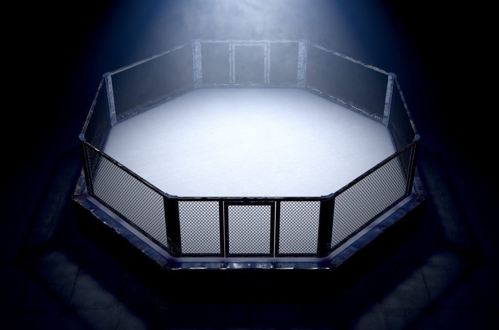 A 3D render of an MMA fight cage arena dressed in black padding spotlit by a single light on an isolated dark background - 3D render