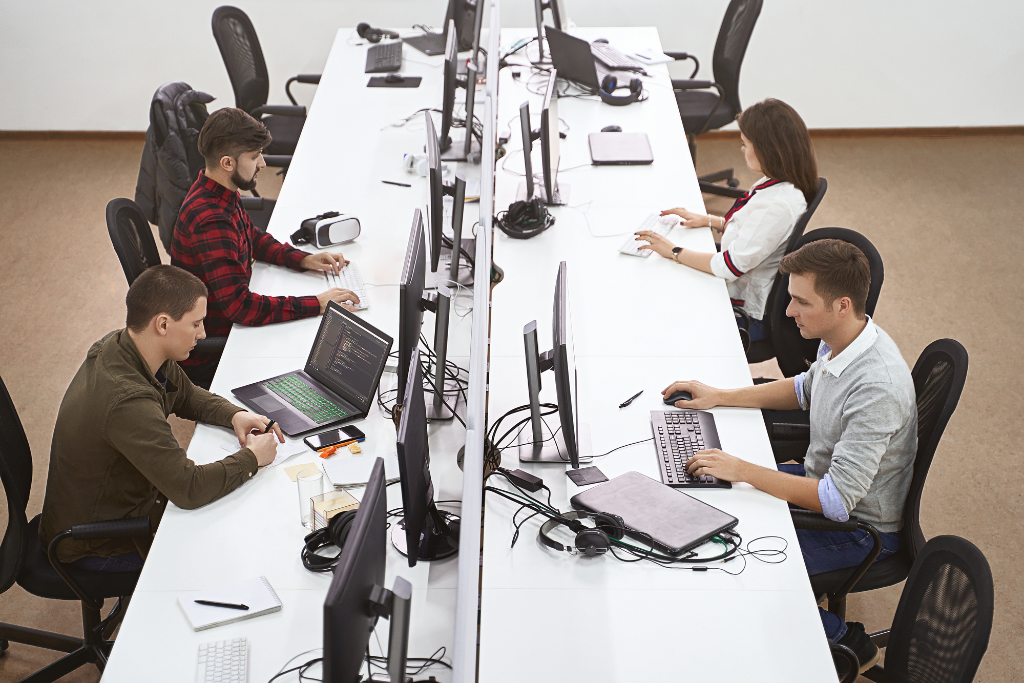Young professionals working in modern office. Group of developers or programmers sitting at desks focused on desktops and laptops in IT company open space. Team at work. High quality image.