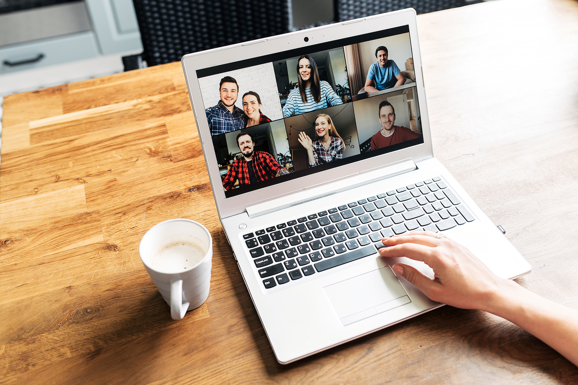 Video call, zoom. Icons of a group of people on laptop screen, app for video online communication. Female hands on the keyboard, cup of coffee near