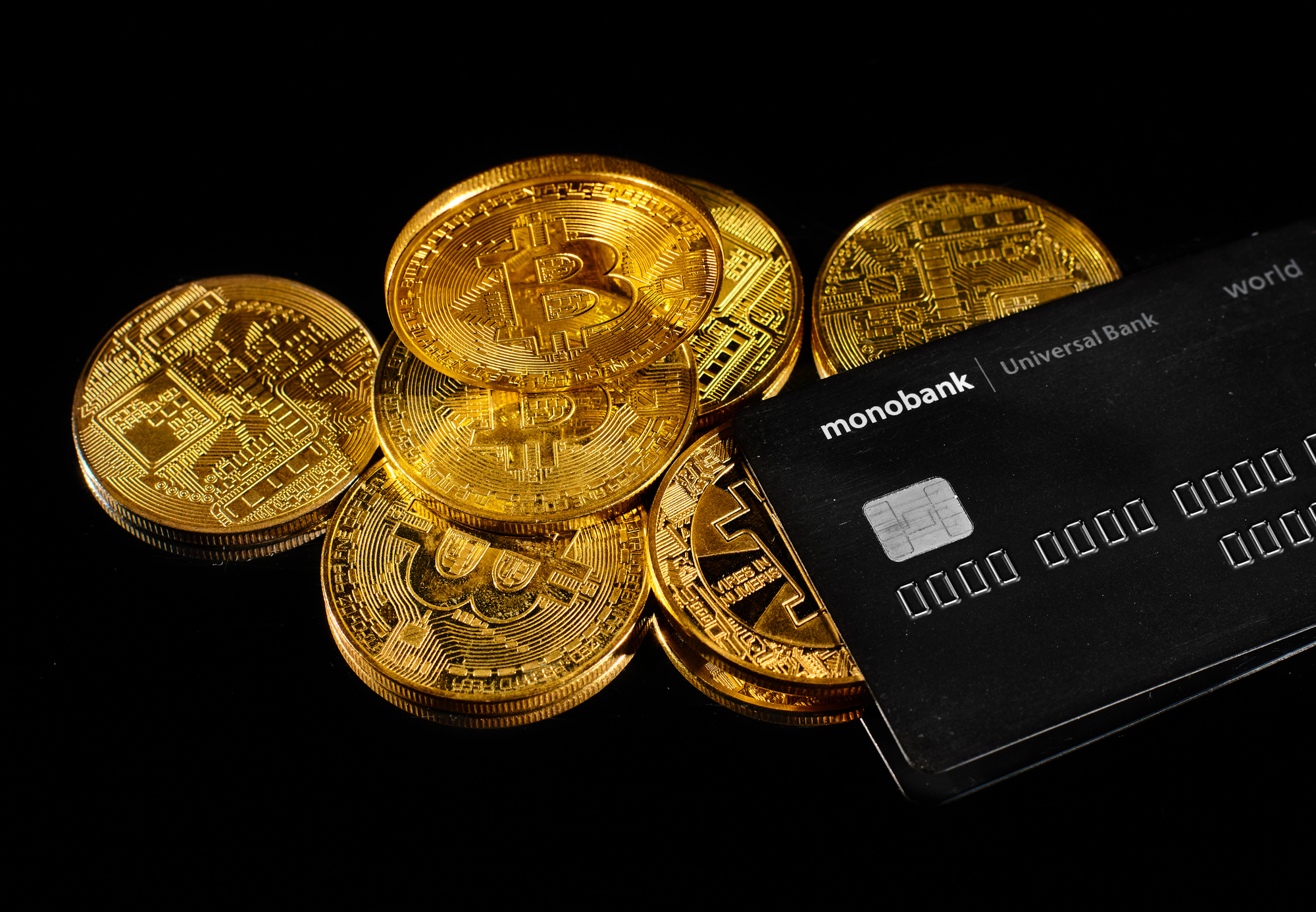 Lutsk, Ukraine - May 1, 2021: Golden coin with bitcoin logo and credit card by monobank. Crypto currency BTC and bitcoin rewards card by Universal bank. E-cash payment or digital electronic money