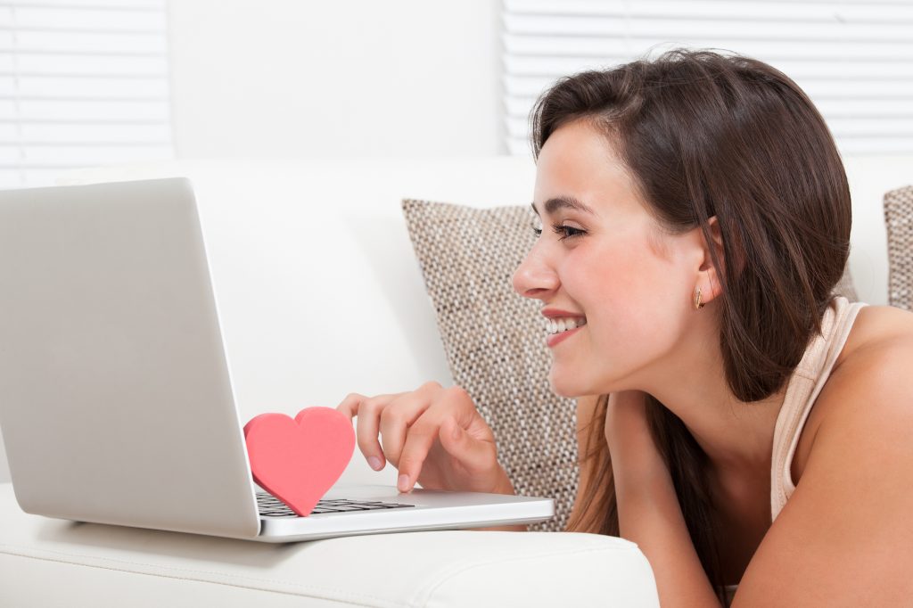 Side view of beautiful young woman dating online on laptop at home