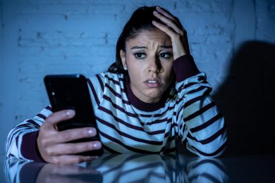 Frightened teenager or young woman using smart mobile cell phone as internet cyberbullying by message stalked abused victim.