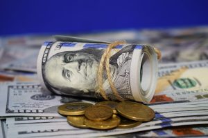 A roll of dollars on the background of scattered hundred dollar bills and various coins. Currency concept.