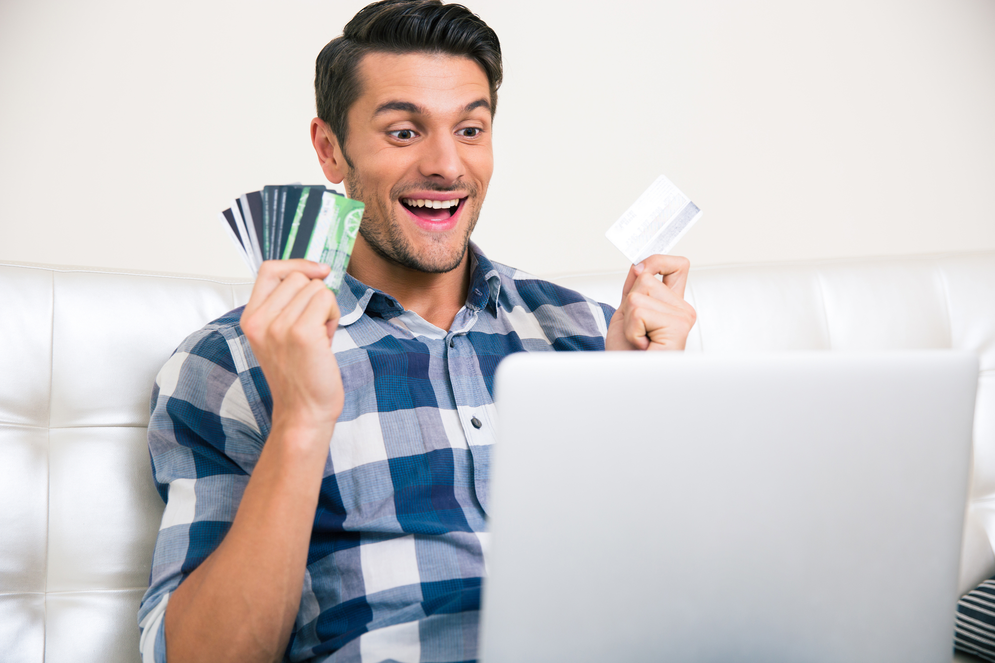 Portrait of a cheerful man holding bank cards and looking on laptop screen at home