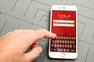 PARIS, FRANCE - SEPT 26, 2016: New iPhone 7 Plus with hand touching screen to sign-in to Tesla Electric car module app. iPhone 7 and iPhone 7 plus is the most wanted phone worldwide