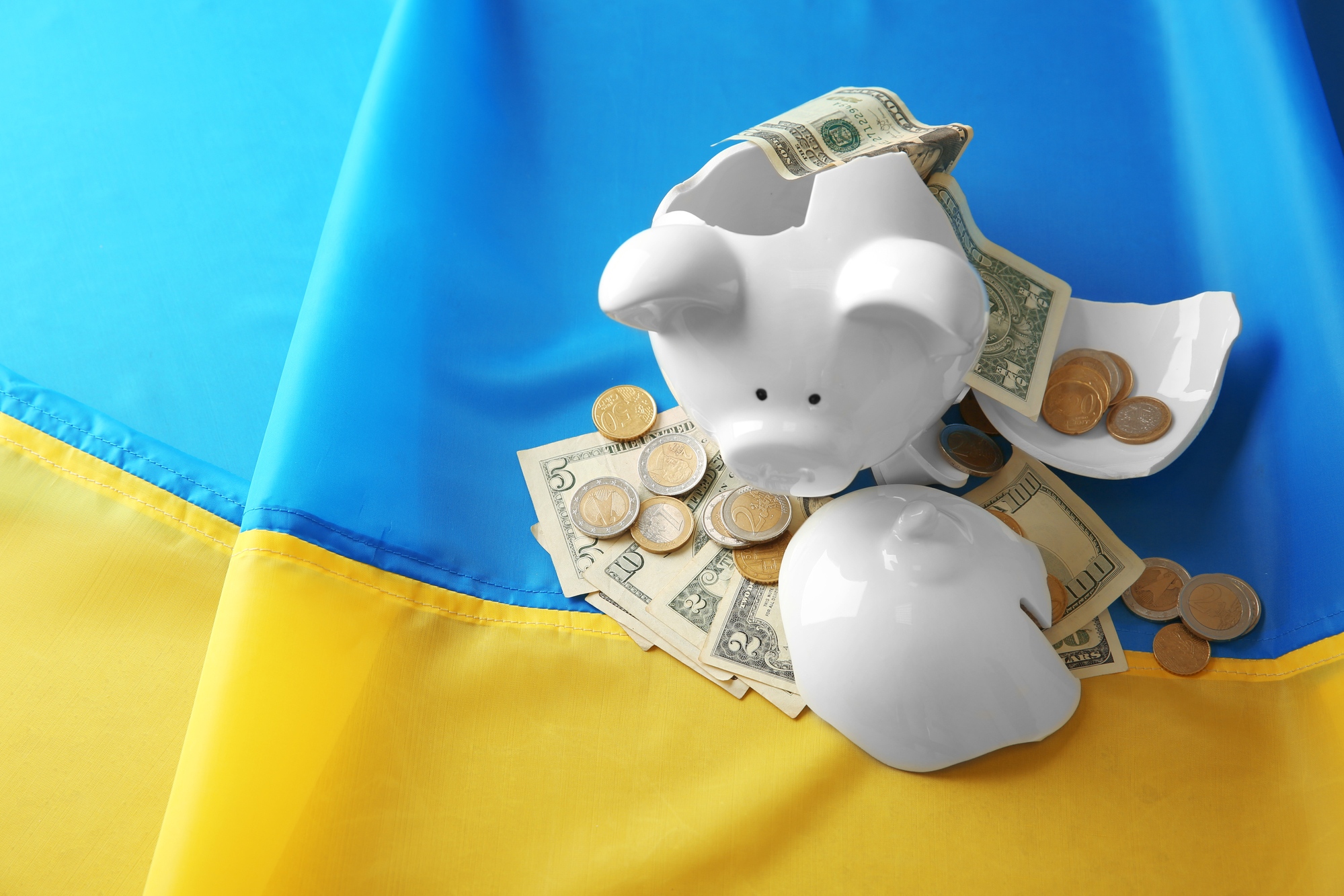 розбита скарбничка з доларами на фоні українського прапору