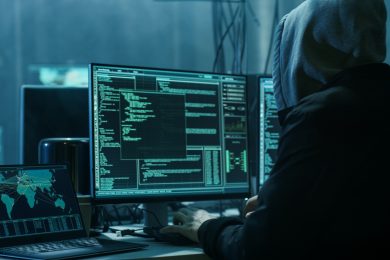 Dangerous Hooded Hacker Breaks into Government Data Servers and Infects Their System with a Virus. His Hideout Place has Dark Atmosphere, Multiple Displays, Cables Everywhere.