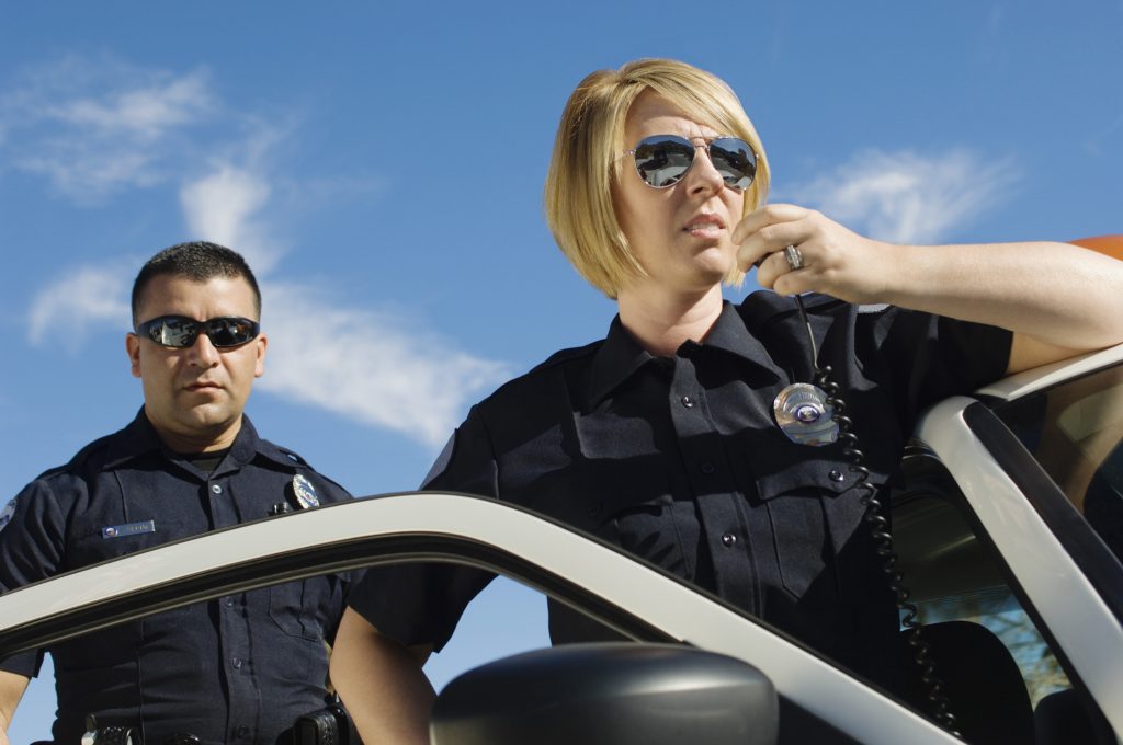 Low angle view of a female police officer communicating on walkie-talkie with coworker in the background against sky