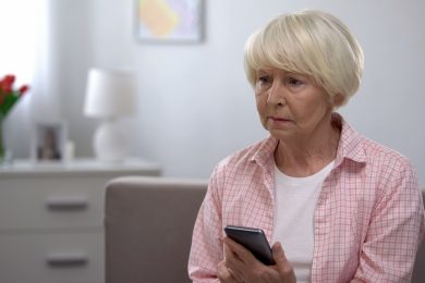 Depressed elderly woman holding smartphone, bad news from relatives, melancholy