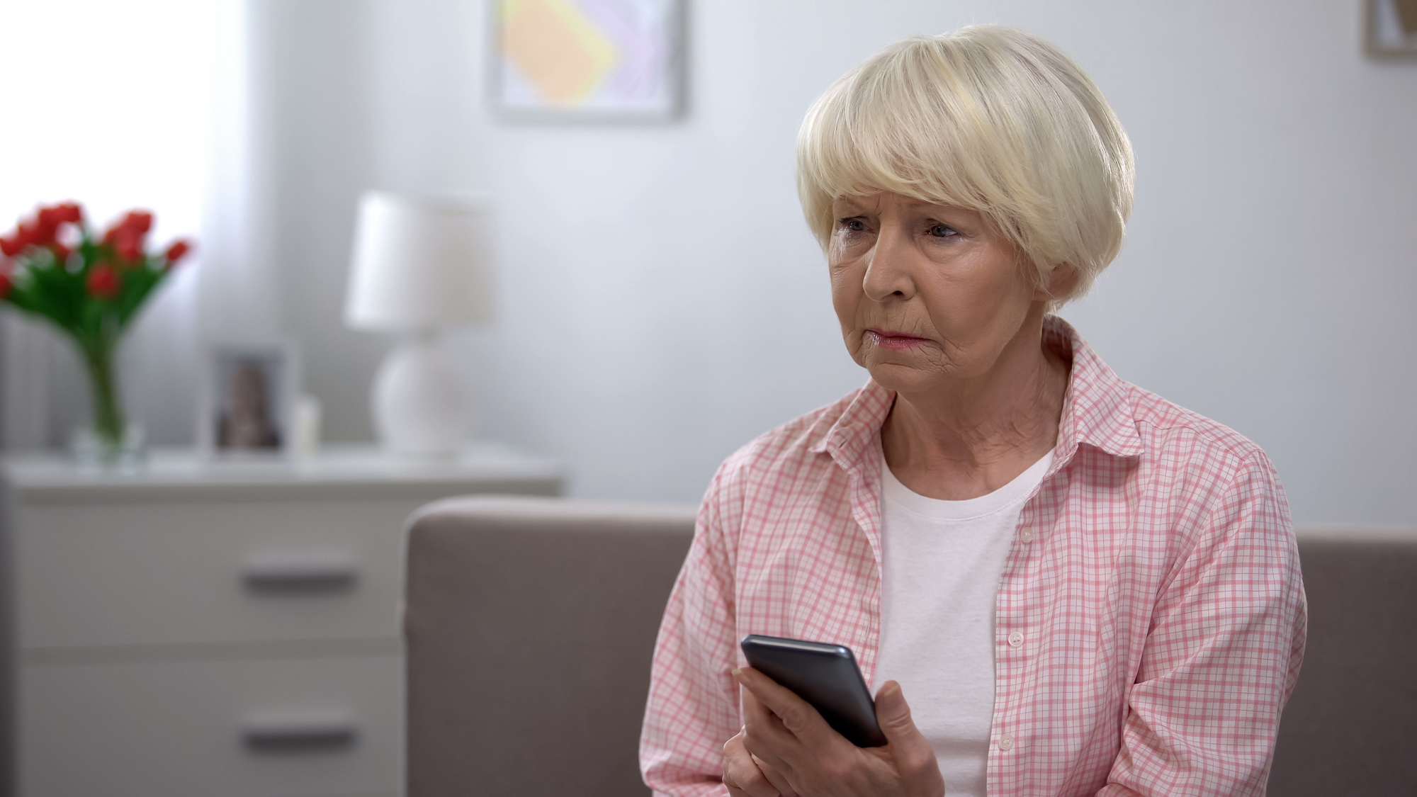 Depressed elderly woman holding smartphone, bad news from relatives, melancholy