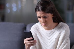 засмучена дівчина в білому светрі дивиться в телефон