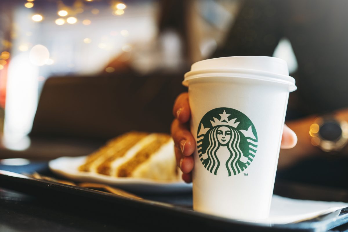 Стакан кави зі Starbucks в руці на фоні тістечка