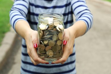 Woman holding money jar with coins outdoors