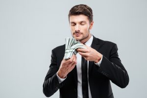 чоловік у чорному костюмі нюхає пачку доларів