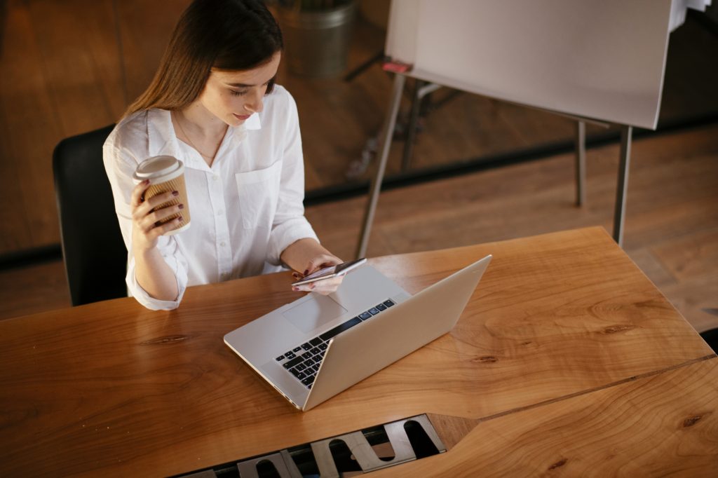 Жінка в білій кофтинці сидить за ноутбуком і п'є каву