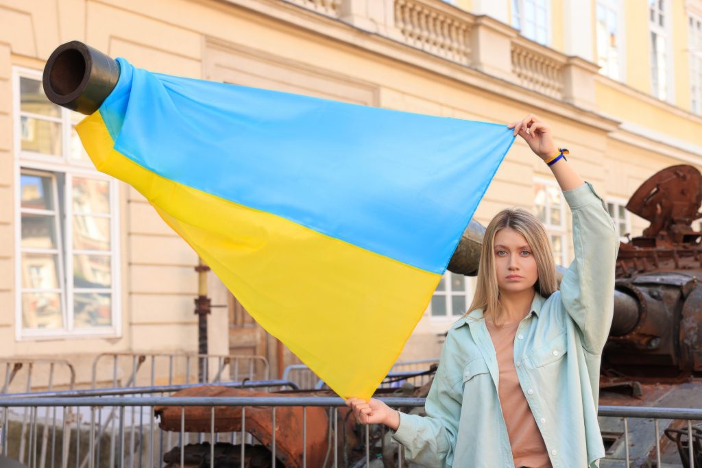 Жінка тримає прапор України на фоні знищеного танка