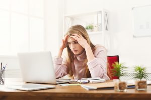 втомлена жінка в рожевому светрі працює за ноутбуком у світлій кімнаті