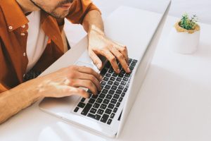 чоловік у коричневій сорочці та білій футболці працює за білим ноутбуком