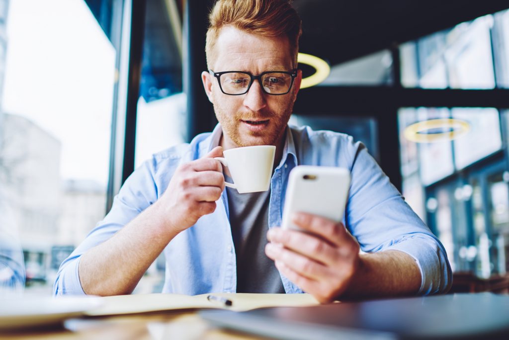 Чоловік п'є каву і дивиться в мобільний телефон