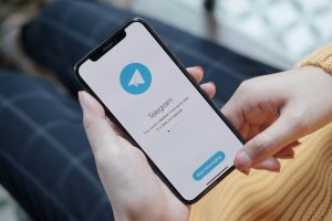 жінка в жовтому светрі тримає телефон з telegram