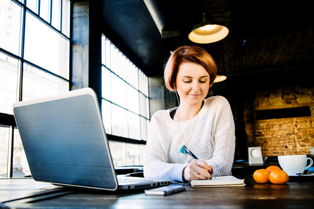 Руда жінка сидить в кафе за ноутбуком