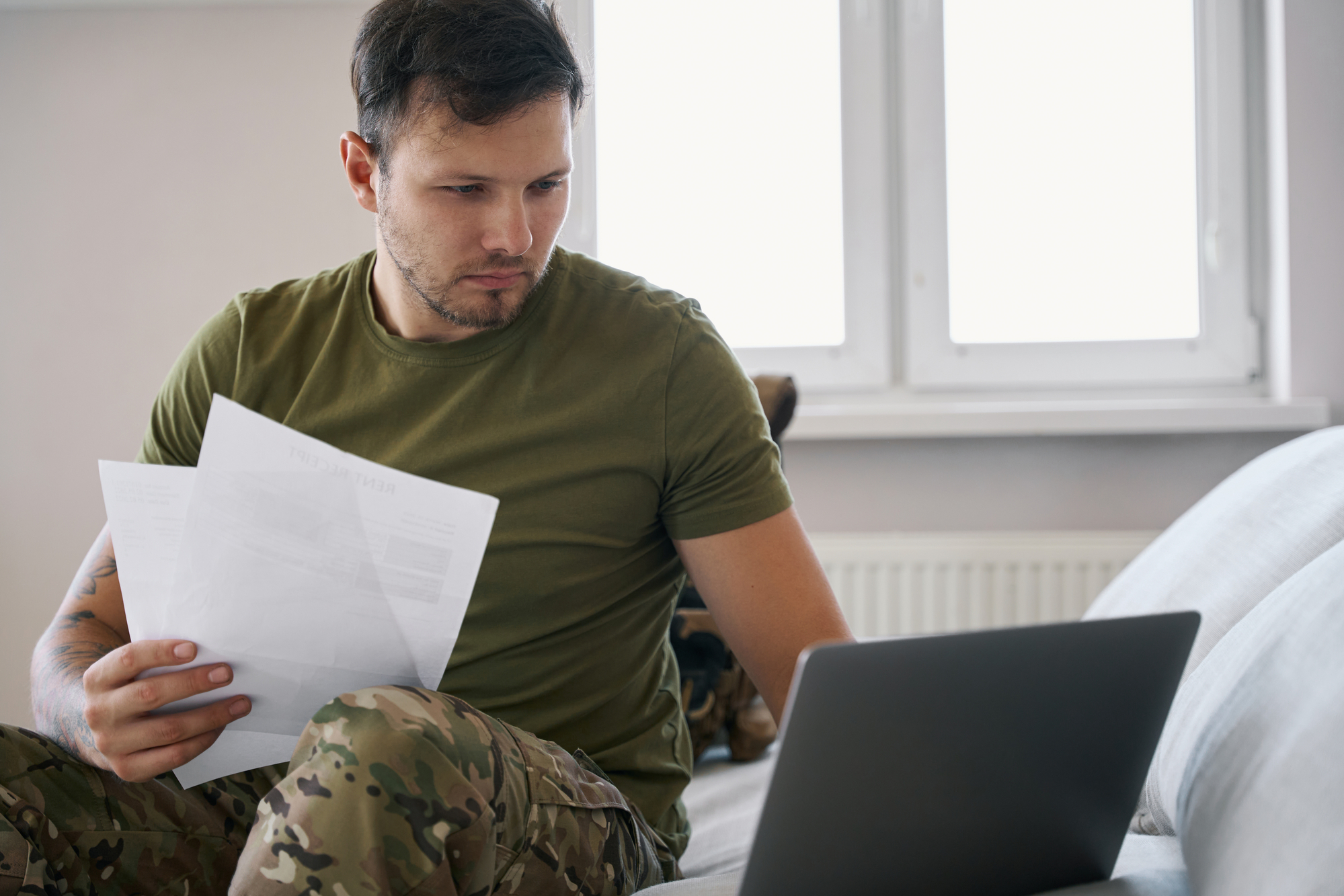 військовий сидить з документами за ноутбуком