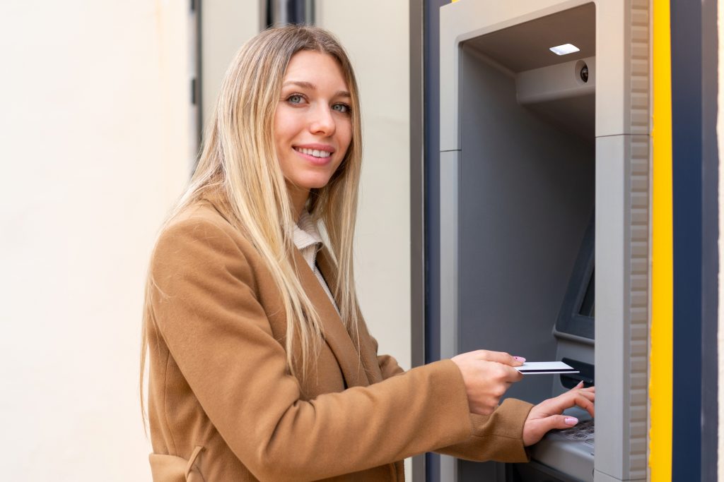 Жінка з білявим волоссям тримає кредитну карту біля банкомата
