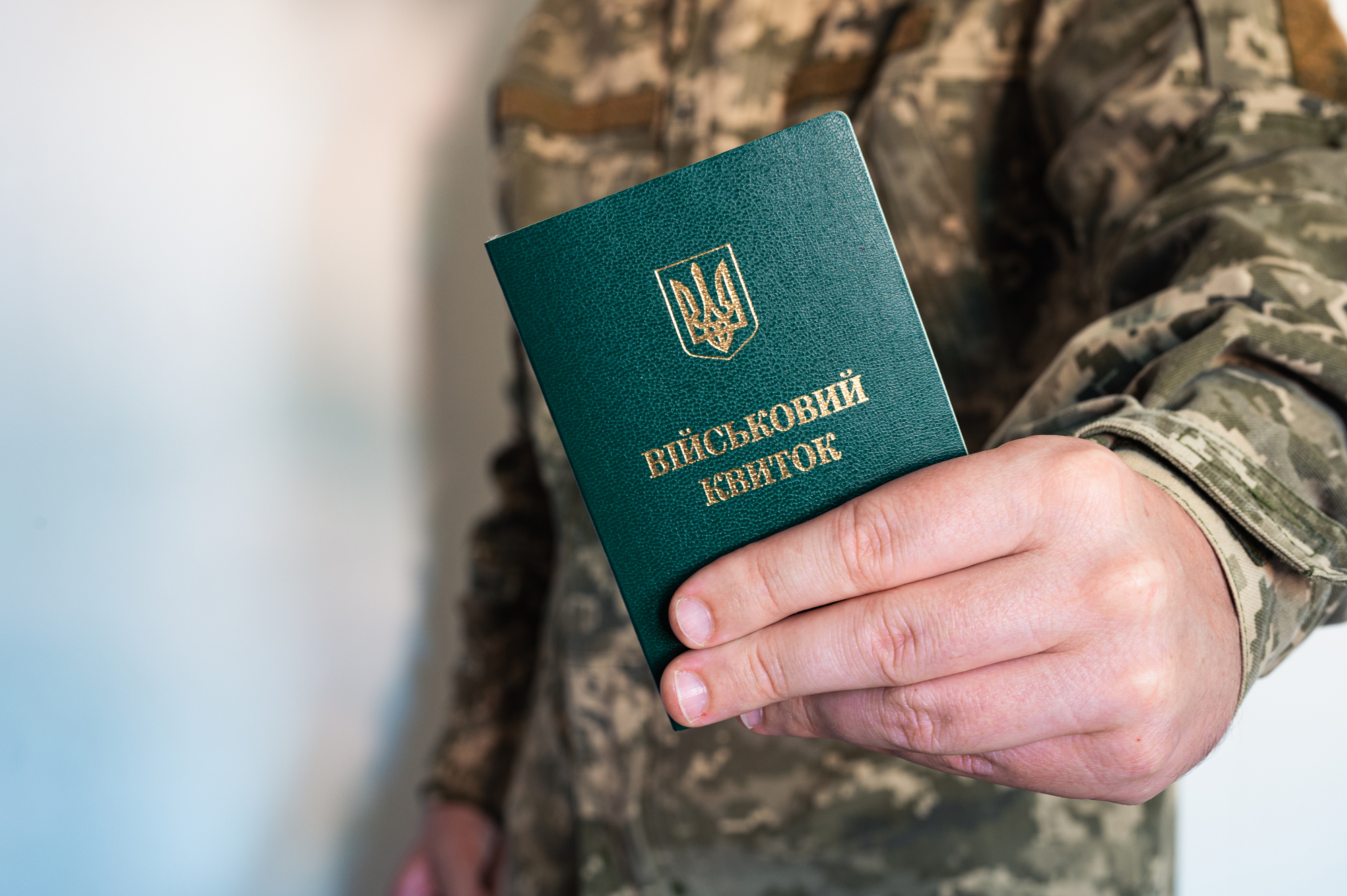 чоловік у військовій формі тримає військовий квиток, зелена книжка