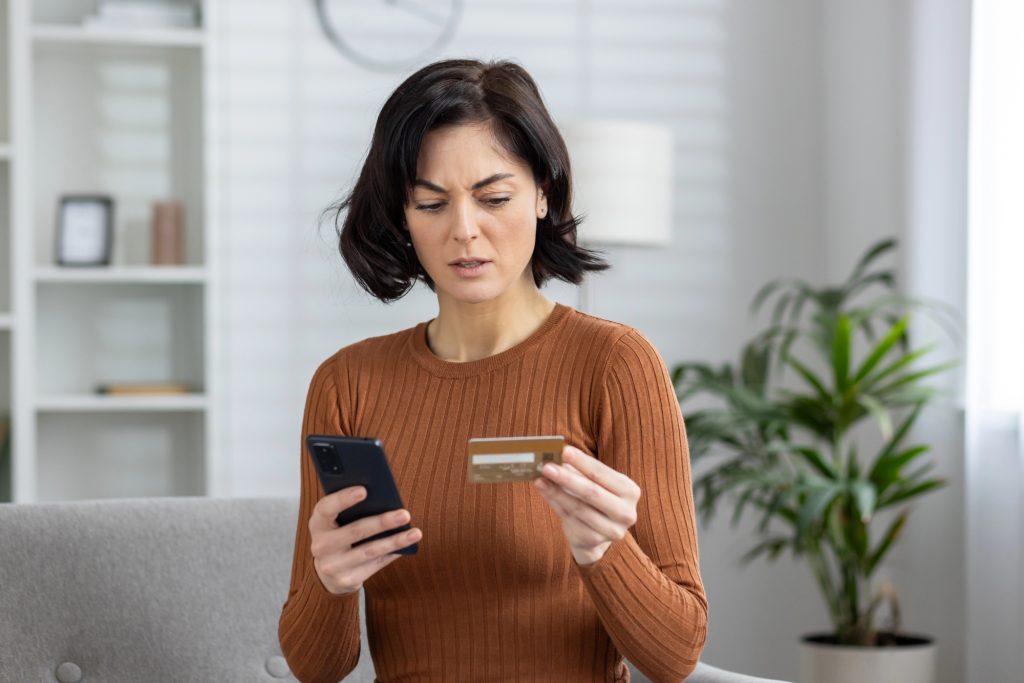 сумна жінка тримає телефон і банківську картку