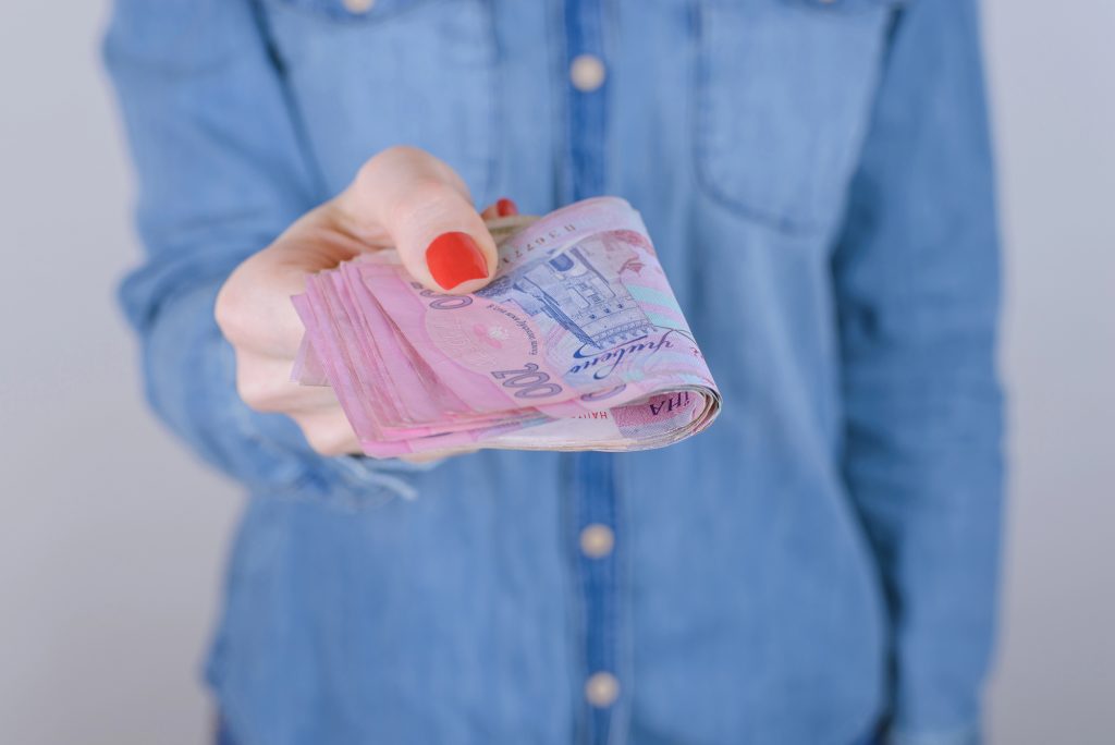 жінка в синій сорочці дає гроші, гривні, купюри по 200 гривень